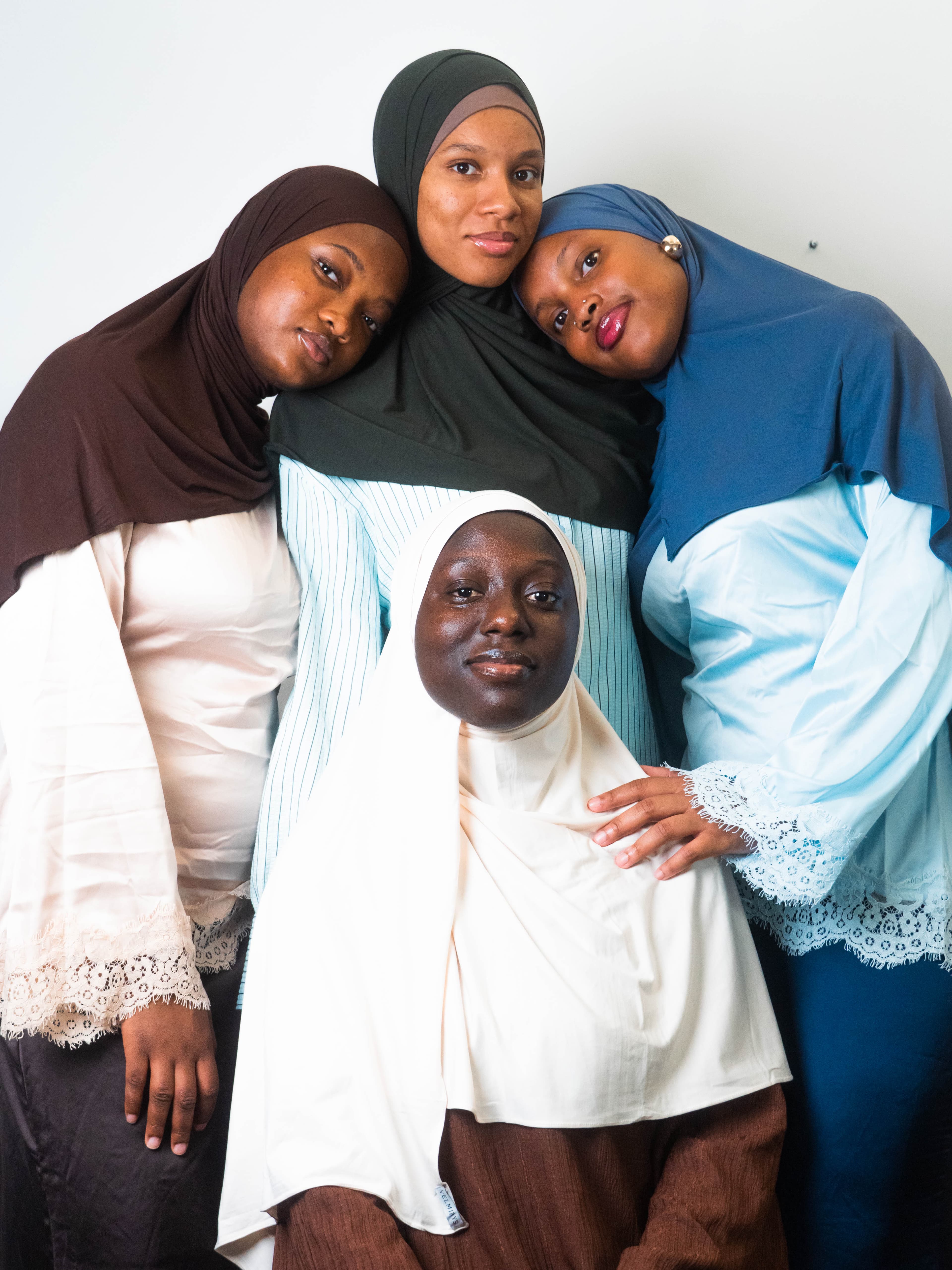 Quatre femmes portant des hijabs VELMIRYS aux teintes douces — bordeaux, vert sauge, bleu ardoise et crème — posant ensemble avec sororité, univers VELMIRYS